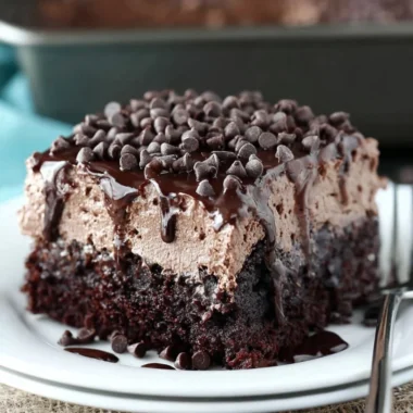 Delicious chocolate poke cake topped with chocolate frosting and chocolate chips.