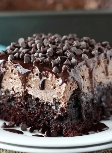 Delicious chocolate poke cake topped with chocolate frosting and chocolate chips.
