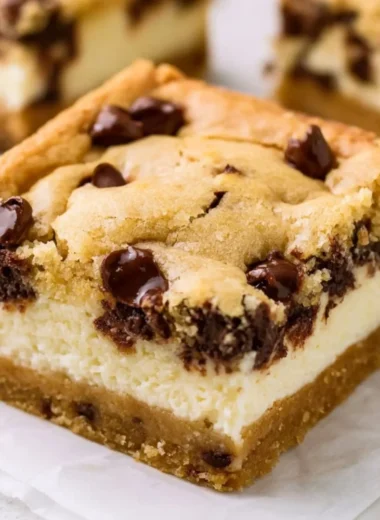 Delicious chocolate chip cheesecake bars topped with chocolate chips and a creamy filling.