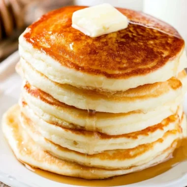Delicious fluffy pancakes stacked on a plate with syrup and berries