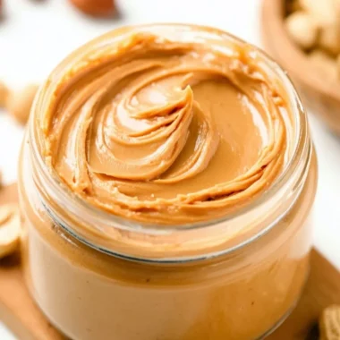 Homemade peanut butter in a jar with a spoon, ideal for spreads and recipes.