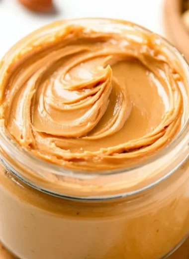 Homemade peanut butter in a jar with a spoon, ideal for spreads and recipes.