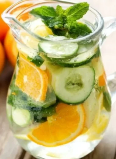 Orange cucumber and mint water in a glass with fresh ingredients around it