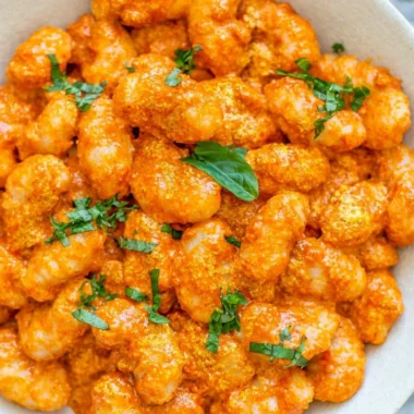 Cozy gnocchi in garlic cream tomato sauce served in a bowl garnished with herbs.