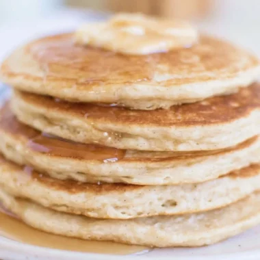 Fluffy sourdough pancakes topped with syrup and berries on a plate